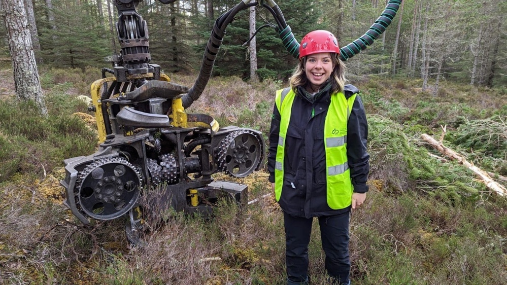 Hannah in front of a harvester head in the forest.