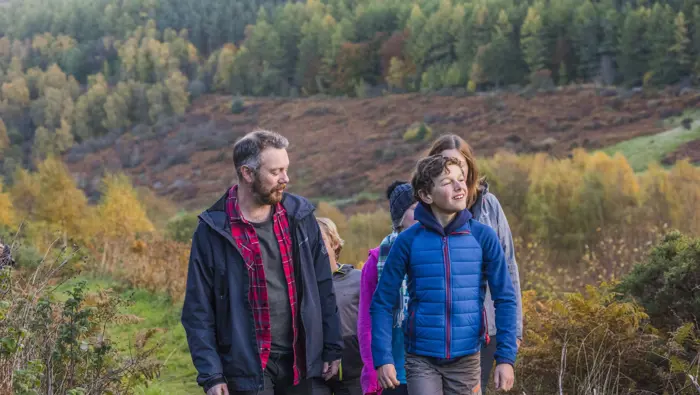 Family walking up a hill with trees in the background.