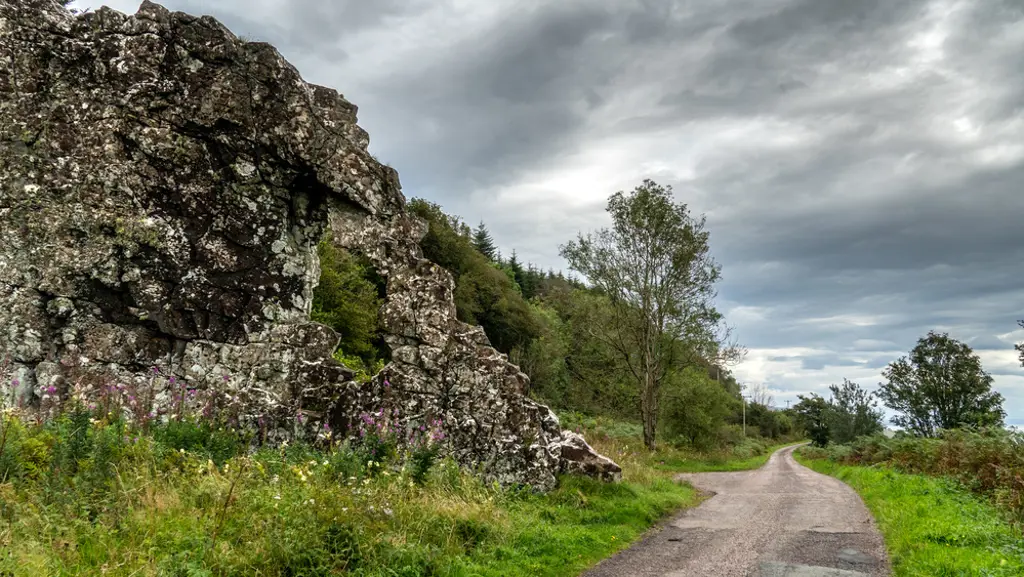 A road next to a large rock formation with a hole in it.