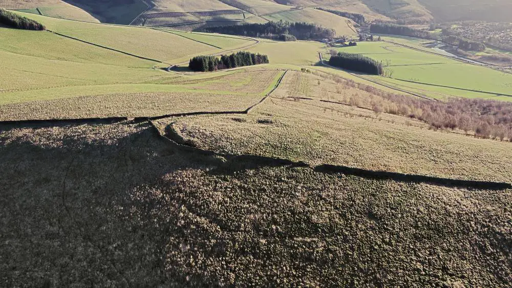 Aerial view of bare green hills with low walls