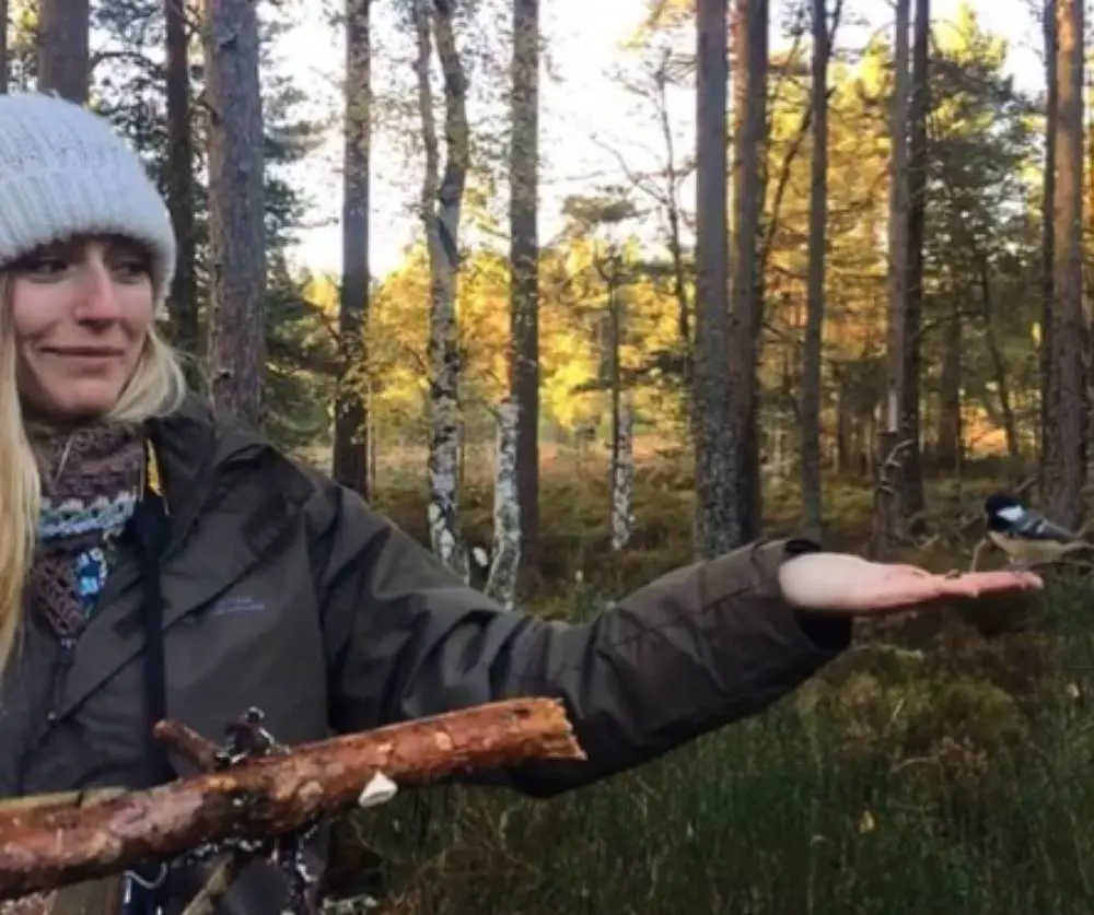 Woman in jacket and beanie hat with hand out in forest setting and sunshine