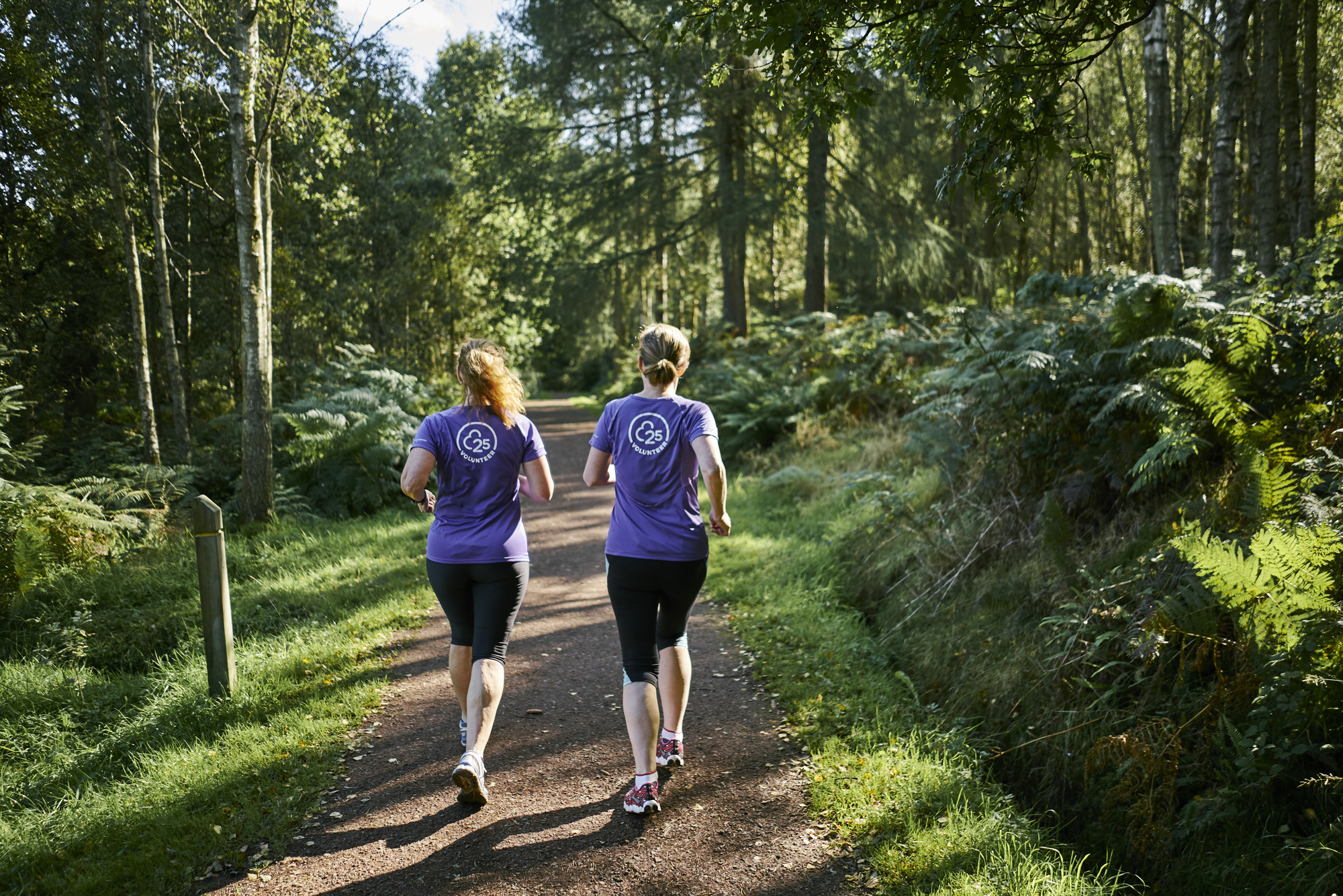 Rear view of two female runners running on tree lined track in Callendar Park parkrun, Falkirk