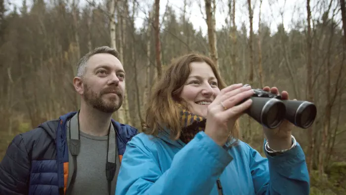 Two people, one with binoculars, looking up. 