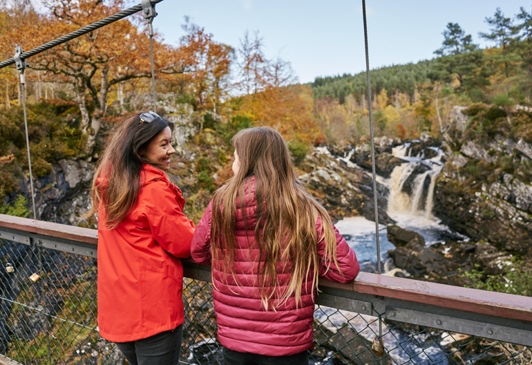 Rear view of woman and teenage girl looking over suspension bridge onto waterfall below, Rogie Falls, near Contin, Black Isle
