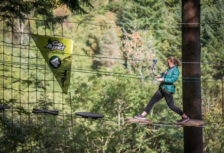 A woman balances on wires above forest at GoApe Treetop Adventures