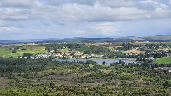 View over a loch with houses, fields and trees surrounding the loch. 