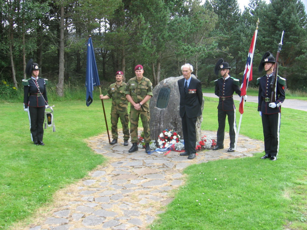 Joachim Rønneberg with five people in military uniforms in front of  the memorial.