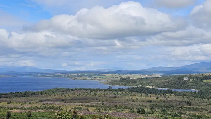 View over a loch with trees and hills in the background.