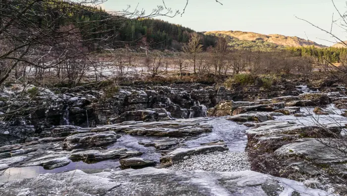Partially frozen waterfall in the foreground with trees in the background.