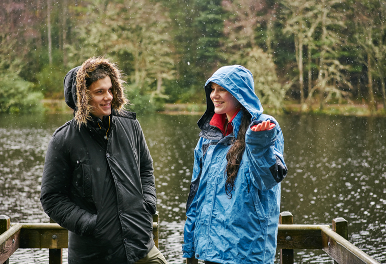 A man and woman in thick waterproof coats stand at the loch side