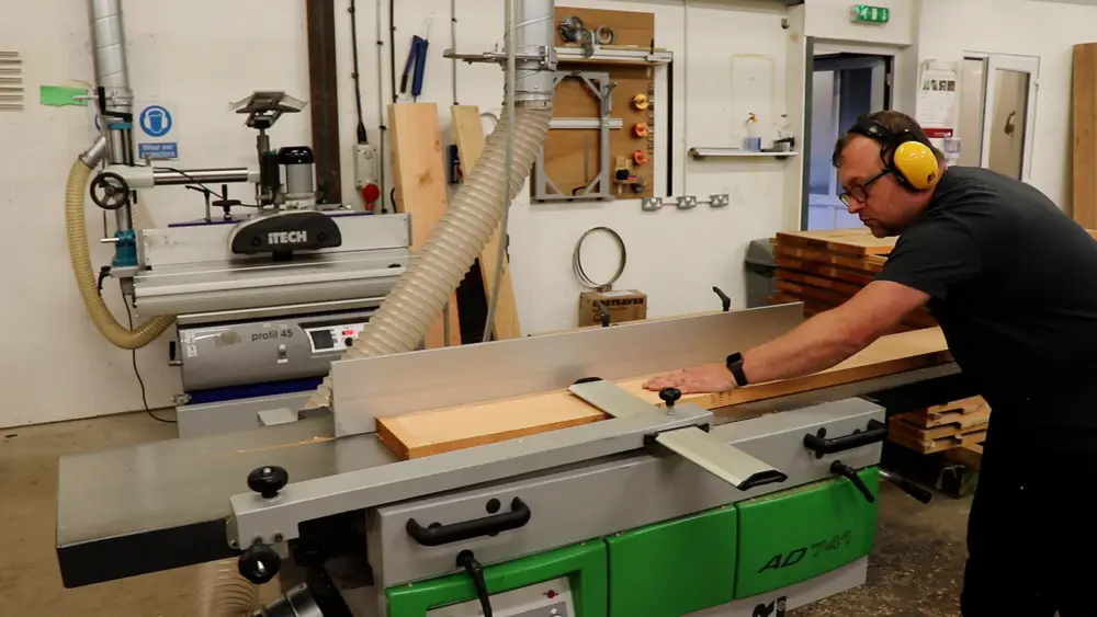 Man pushing a wooden board across a large machine