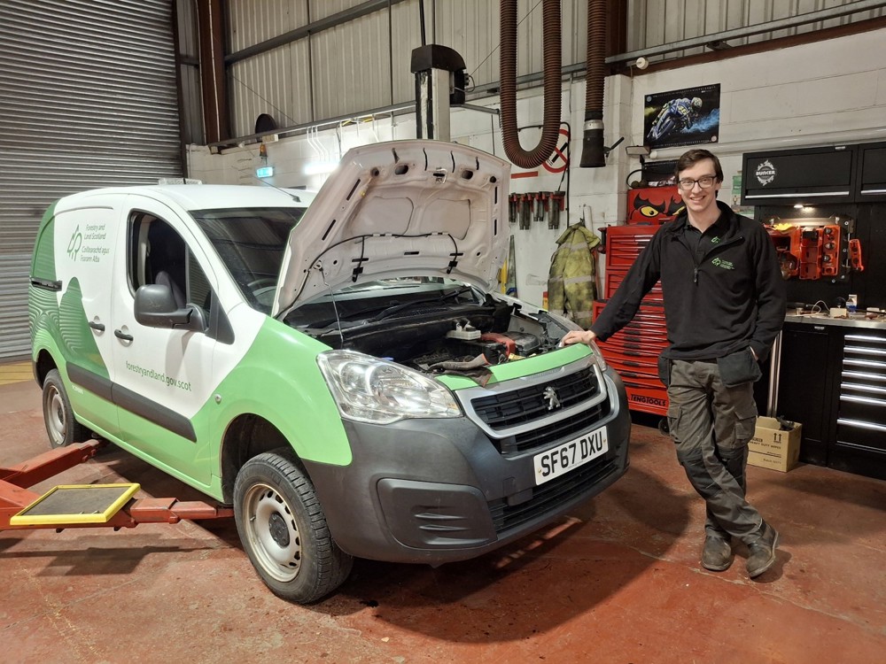 Kyle stood next to a van with the bonnet raised.