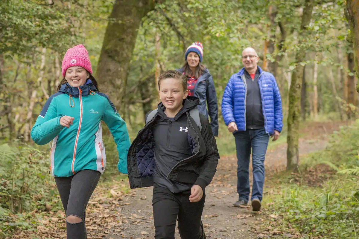 Boy and girl running along woodland path, their parents behind them