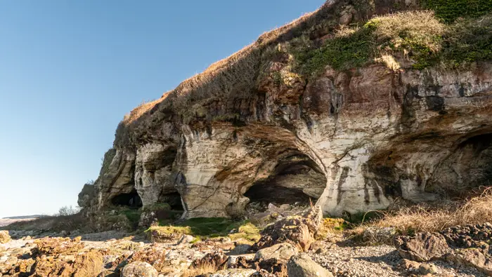A cave inside a rocky shoreline with grass ontop