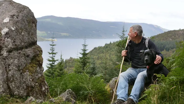 Man and dog sitting with Loch Ness in the background.