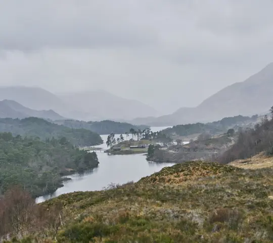 View from high viewpoint on heather covered moorland looking overforests and to Loch Affric with panoramic view of surrounding mountain range in the mist in distance, on a cloudy and grey day, Glen Affric