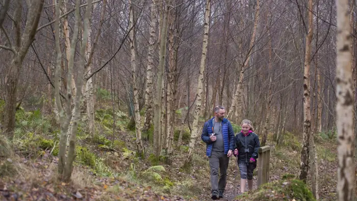 Adult and child walking along a forest path.