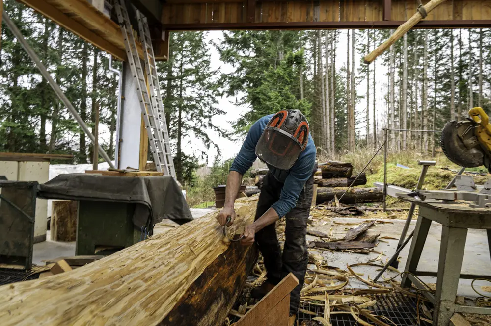 A man shaving the bark off a tree in a wooden workshop