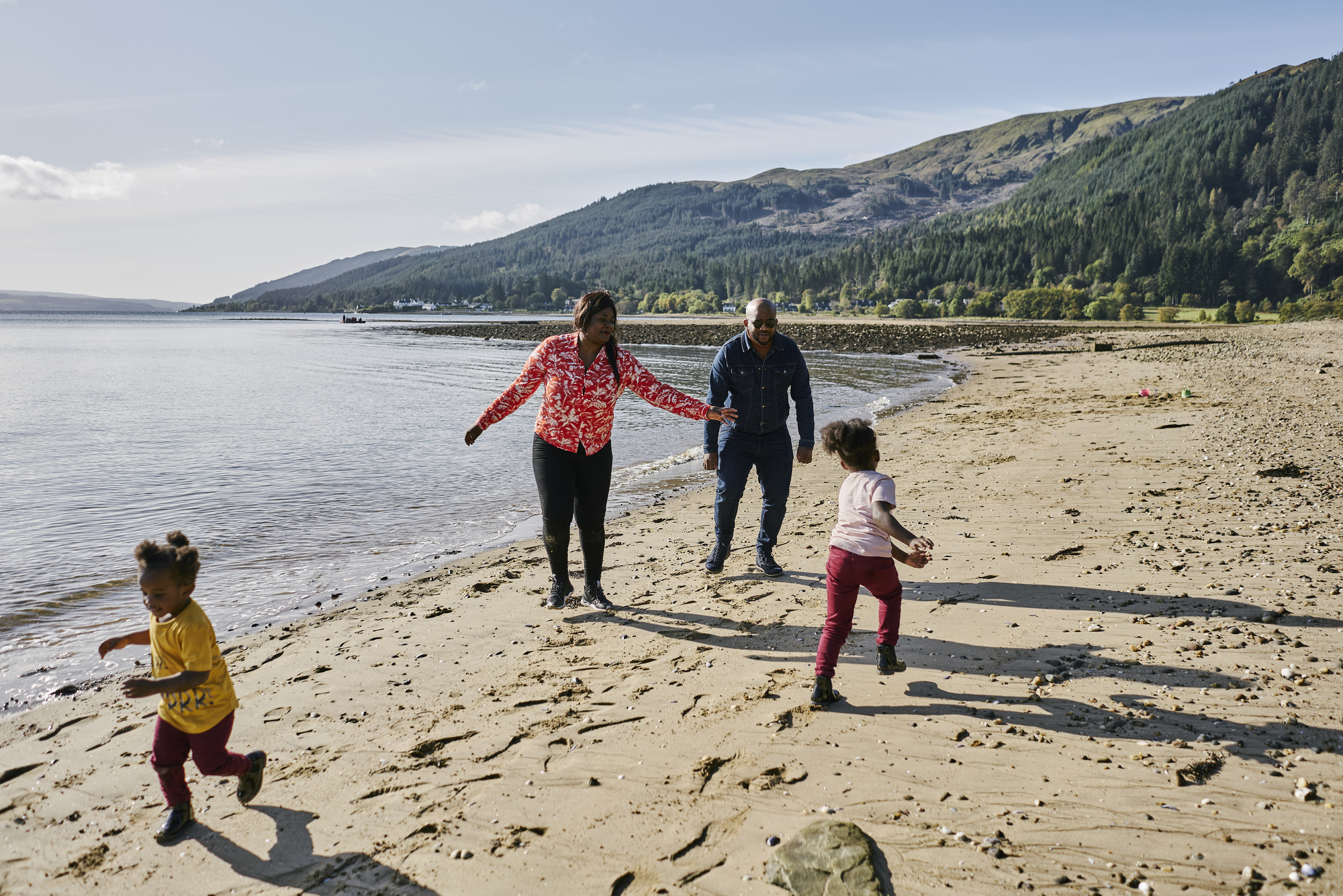 Man, woman and two young girls play run around on beach at Ardentinny, on the shore of Loch Long