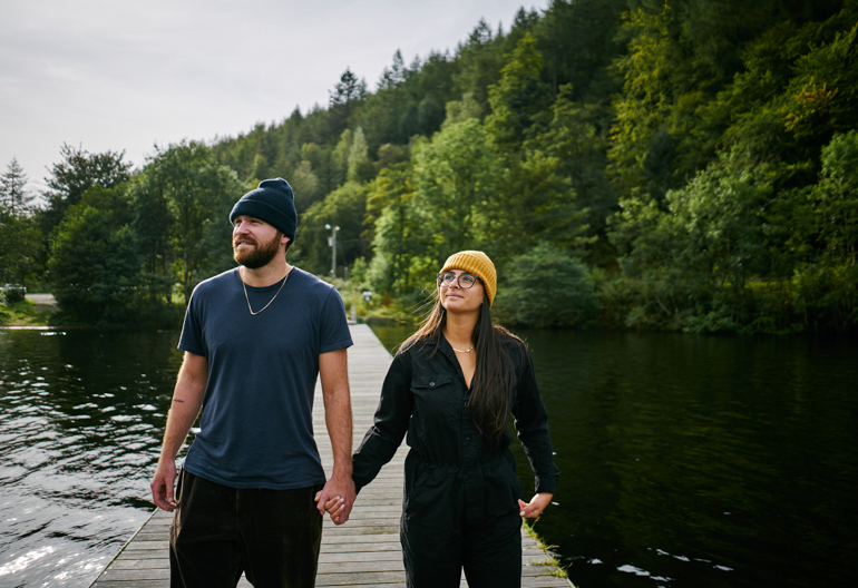Man and woman walk hand in hand along wooden jetty, protruding into Loch Oich, near Fort William
